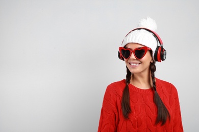 Young woman listening to music with headphones on grey background, space for text