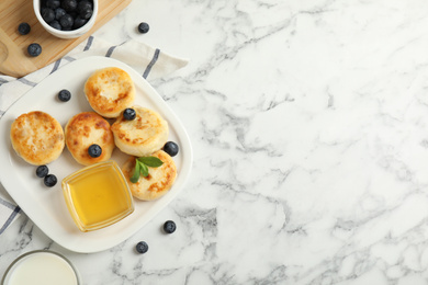 Photo of Delicious cottage cheese pancakes with blueberries and honey on white marble table, flat lay. Space for text