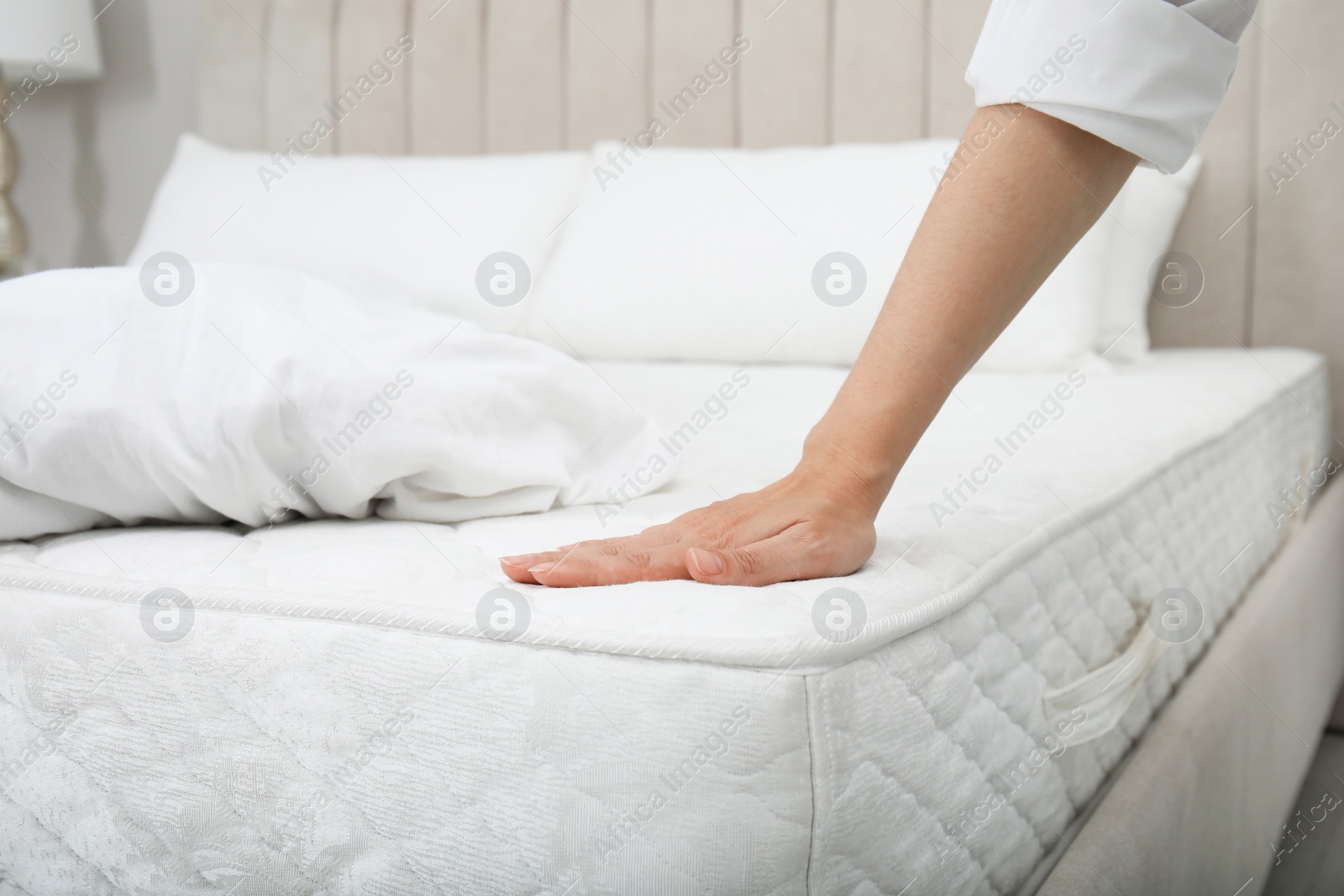 Photo of Woman touching soft white mattress on bed indoors, closeup