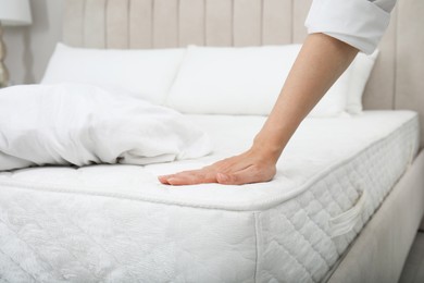 Woman touching soft white mattress on bed indoors, closeup