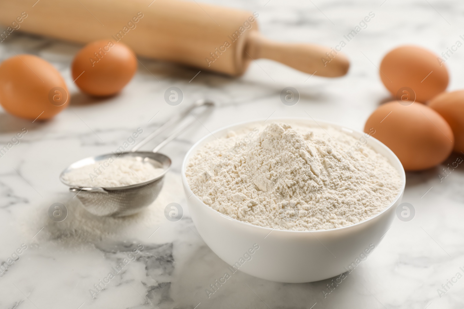 Photo of Bowl of flour and eggs on white marble table