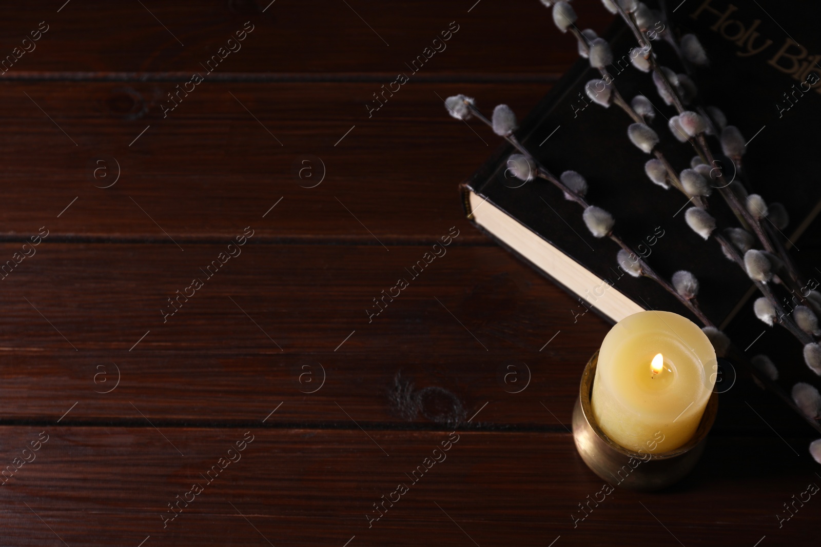 Photo of Bible, burning candle and willow branches on wooden table, above view. Space for text