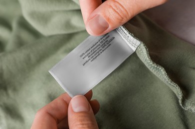Photo of Woman holding clothing label on olive garment, closeup
