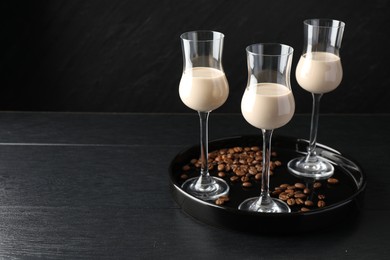 Photo of Coffee cream liqueur in glasses and beans on black wooden table, space for text