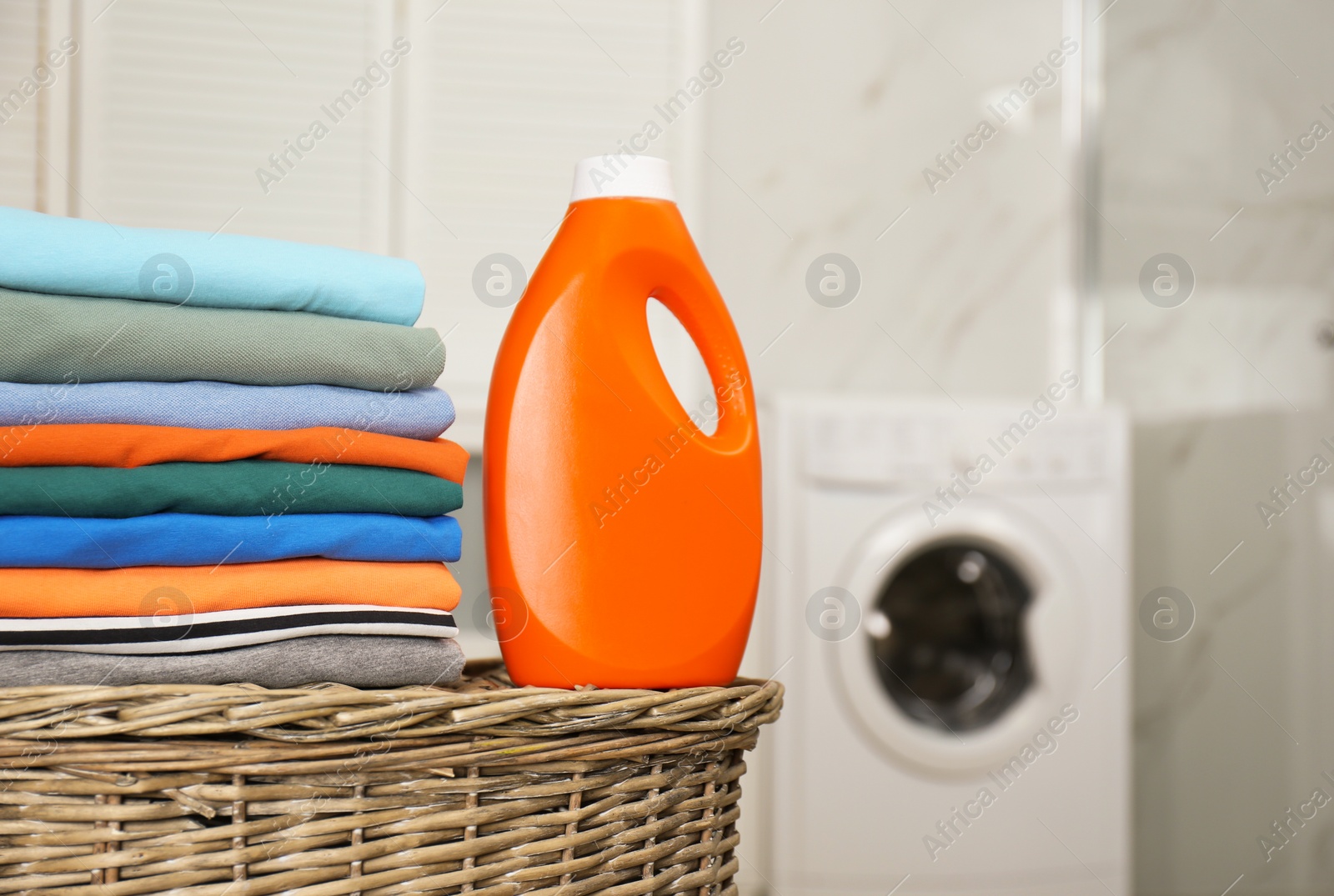 Photo of Fresh laundry and detergent on basket in bathroom. Space for text