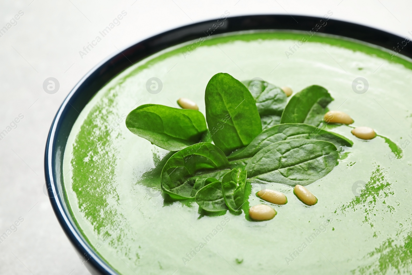 Photo of Bowl of healthy green soup with fresh spinach on grey table, closeup view