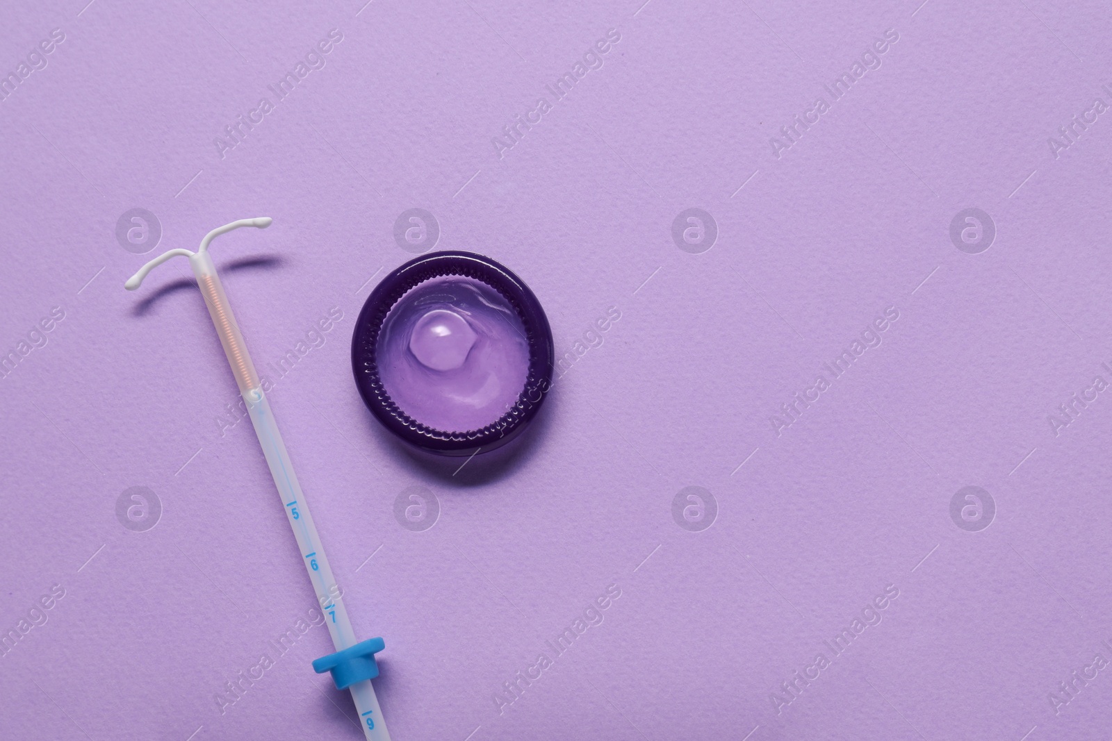 Photo of Condom and intrauterine device on lilac background, flat lay and space for text. Choosing method of contraception