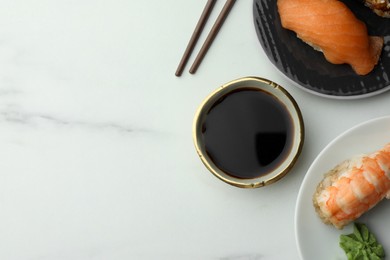 Photo of Tasty soy sauce in bowl, sushi and chopsticks on white marble table, flat lay. Space for text