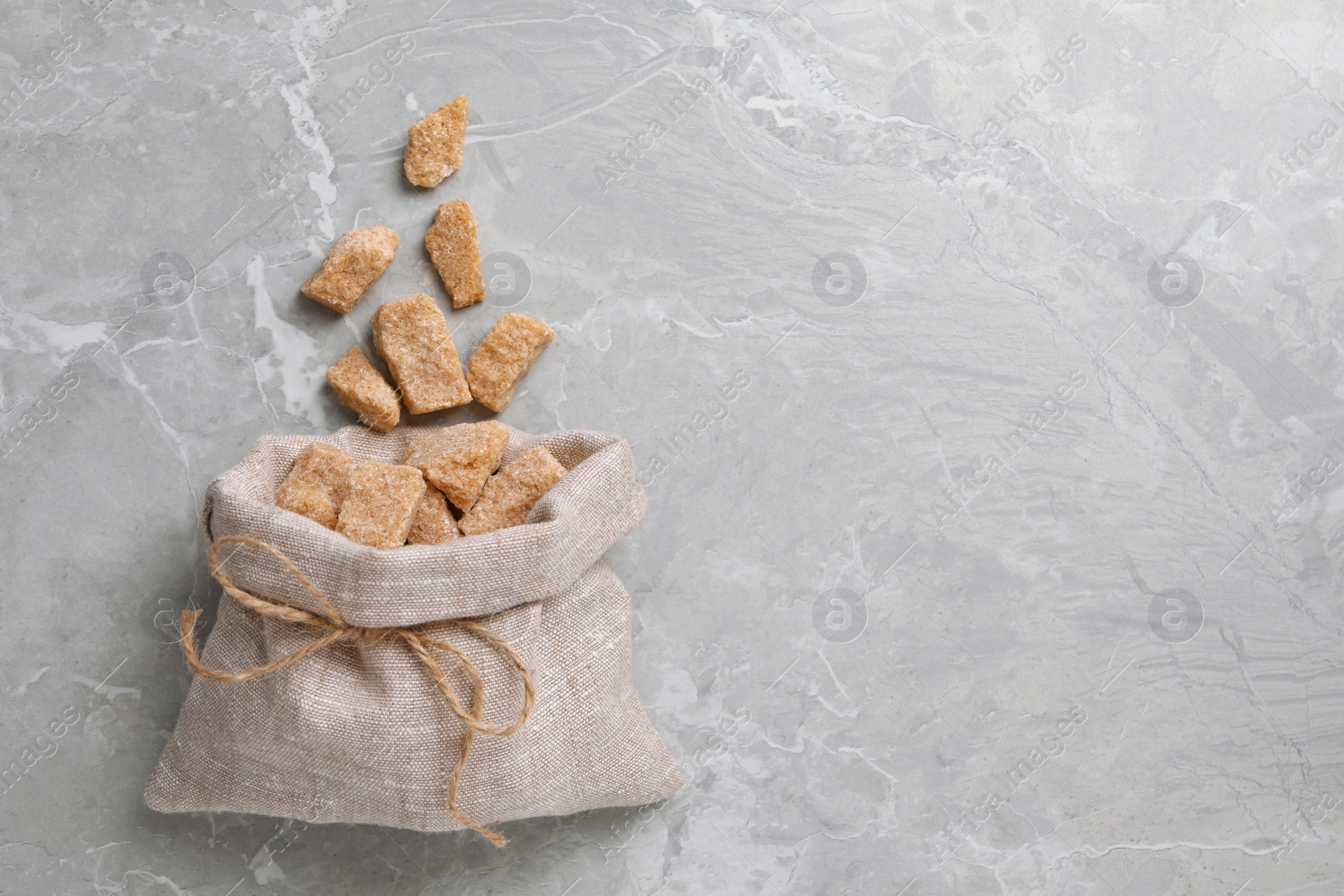 Photo of Bag of brown sugar pieces on light grey marble table, flat lay. Space for text