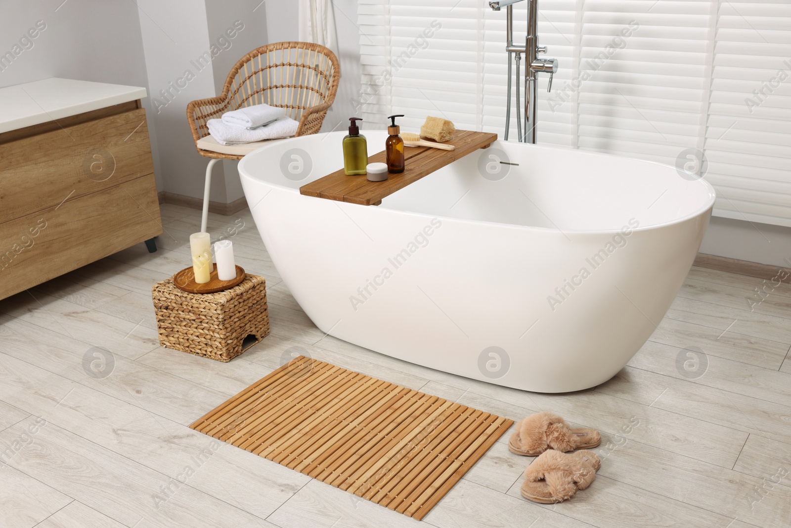 Photo of Stylish bathroom interior with bamboo bath mat and white tub