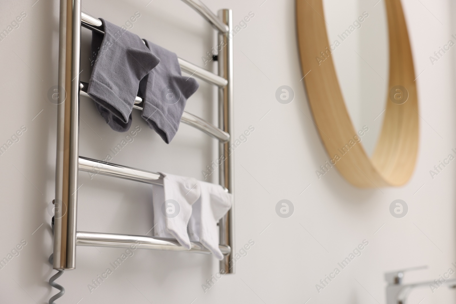 Photo of Heated towel rail with socks on white wall in bathroom