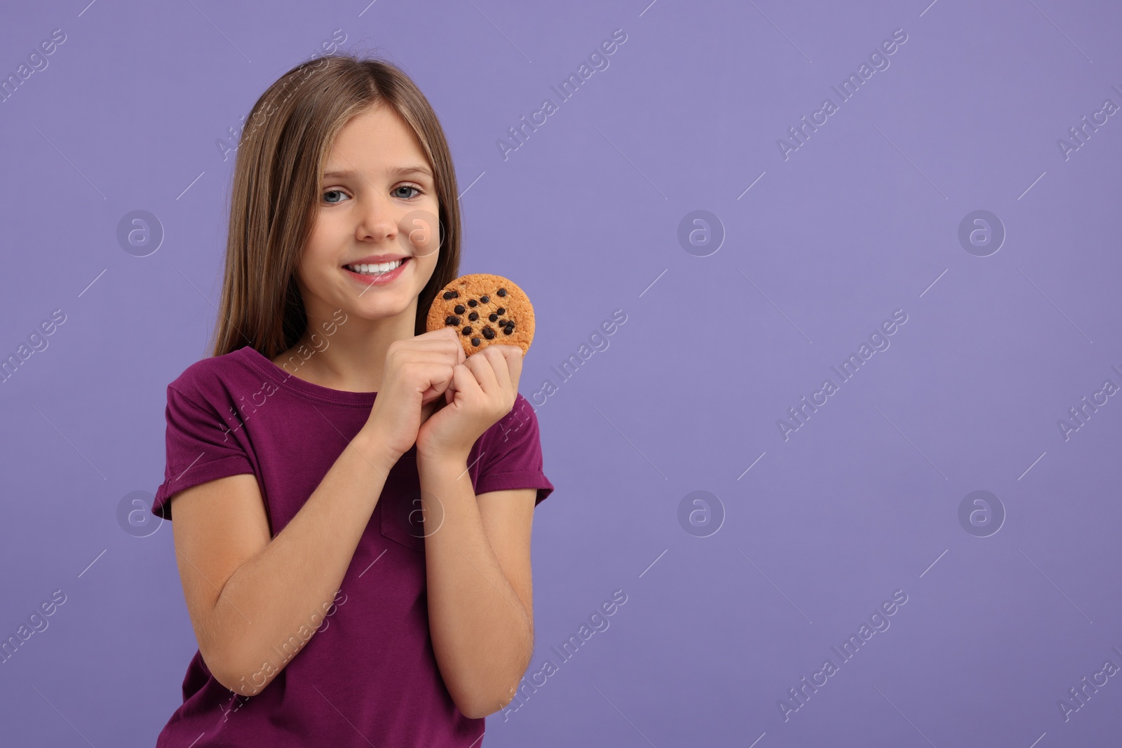 Photo of Cute girl with chocolate chip cookie on purple background. Space for text