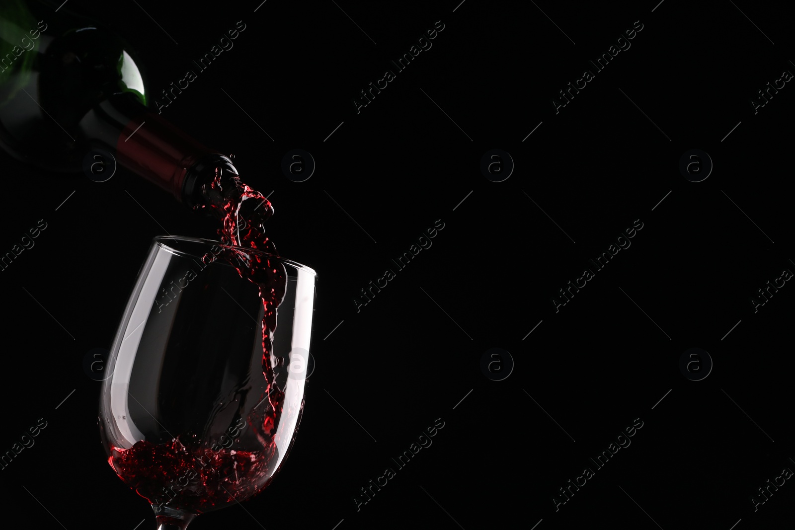 Photo of Pouring tasty red wine from bottle into glass on black background, closeup. Space for text