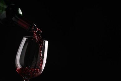 Pouring tasty red wine from bottle into glass on black background, closeup. Space for text