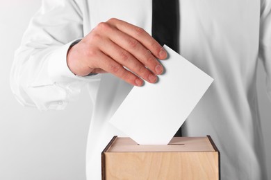 Photo of Man putting his vote into ballot box on light grey background, closeup