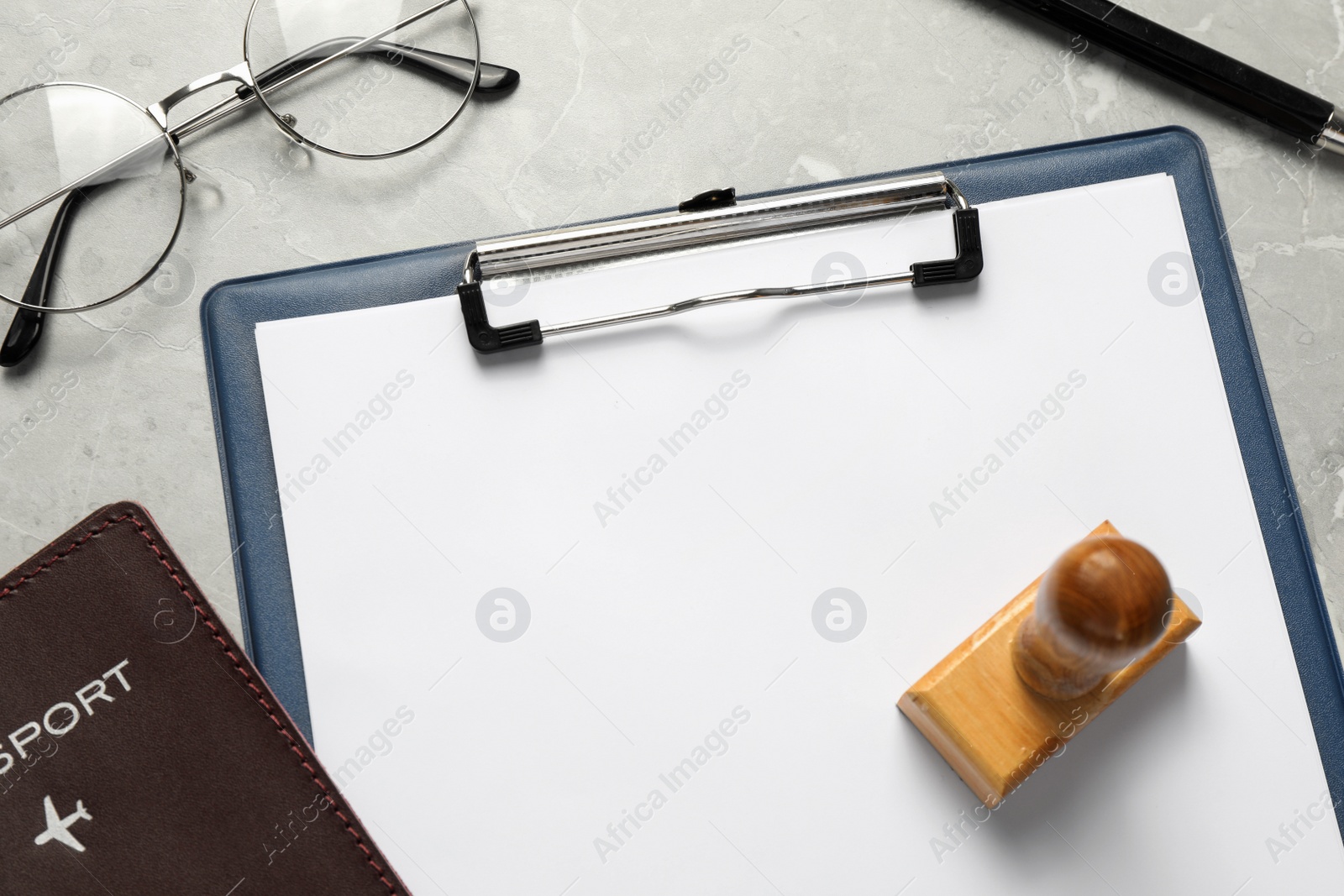 Photo of Clipboard with blank sheet of paper, glasses, passport and wooden stamp on light grey table