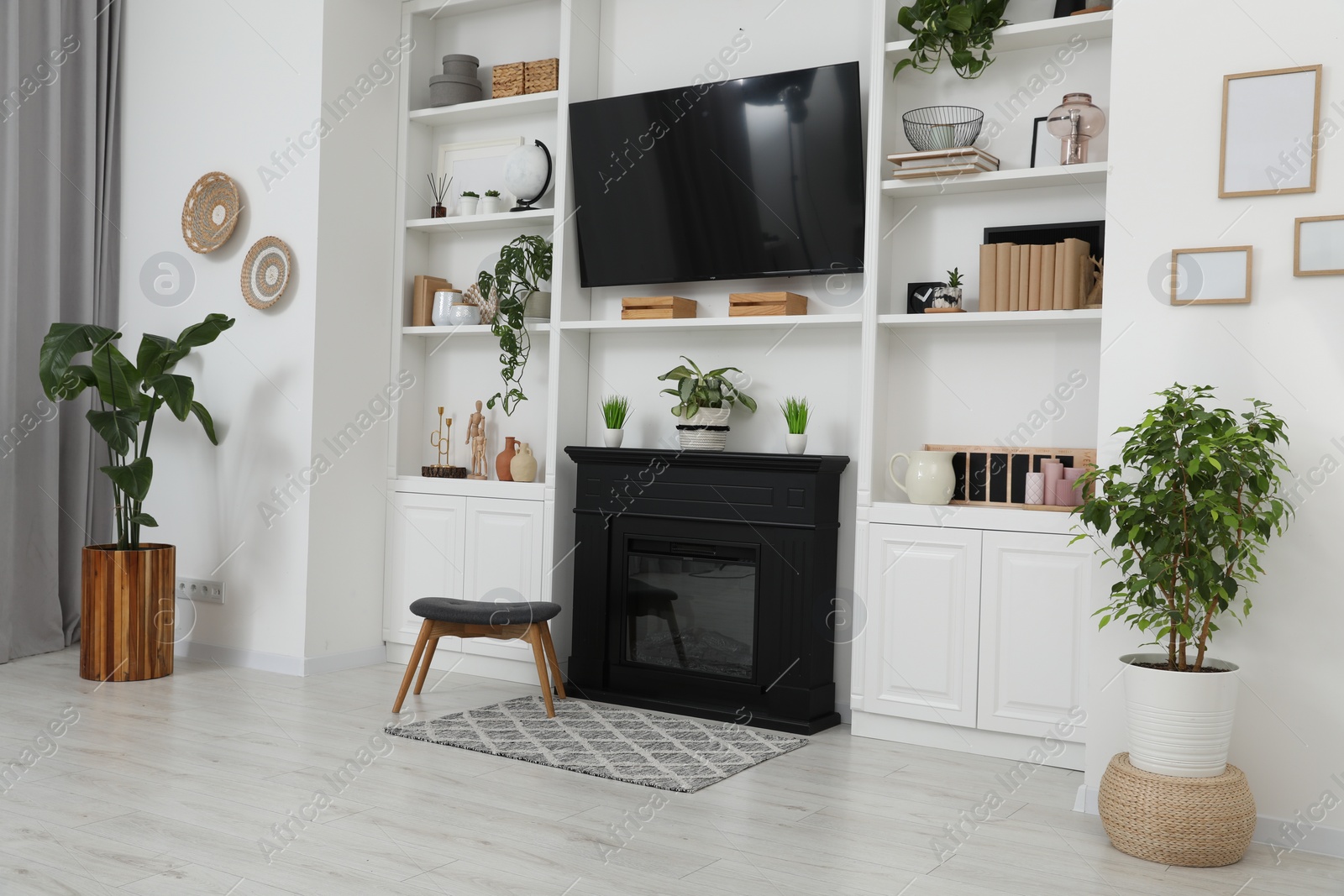 Photo of Stylish room interior with beautiful fireplace, TV set and shelves with decor and houseplants
