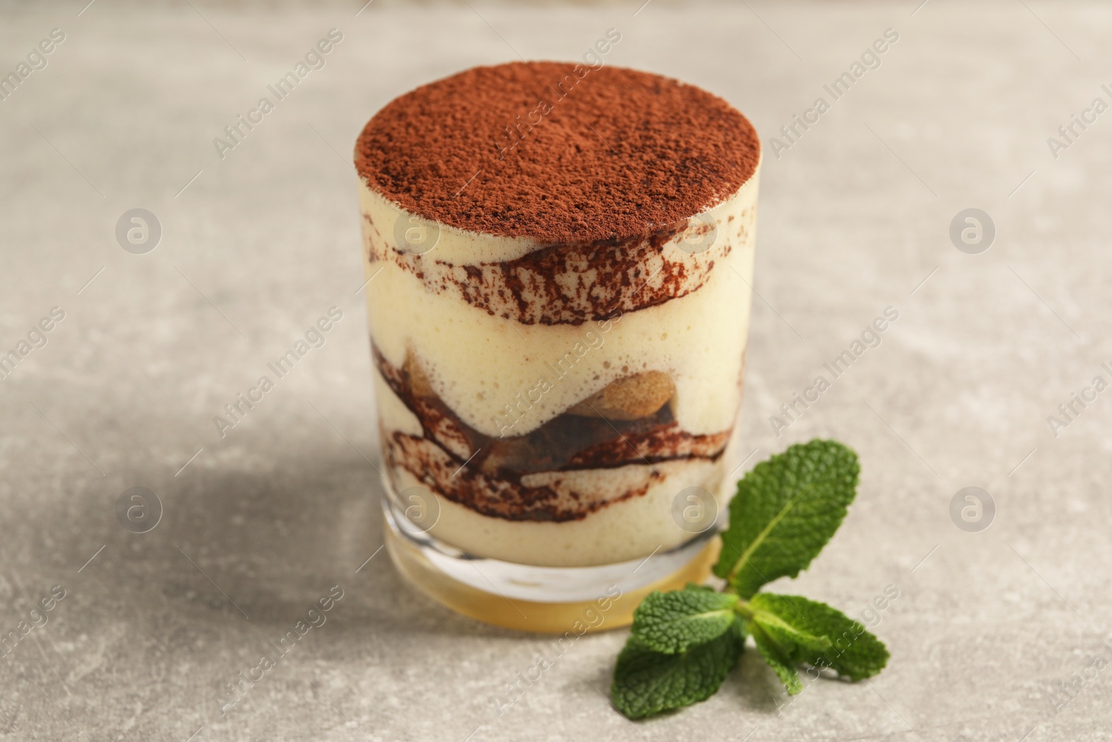 Photo of Delicious tiramisu in glass and mint on grey textured table, closeup