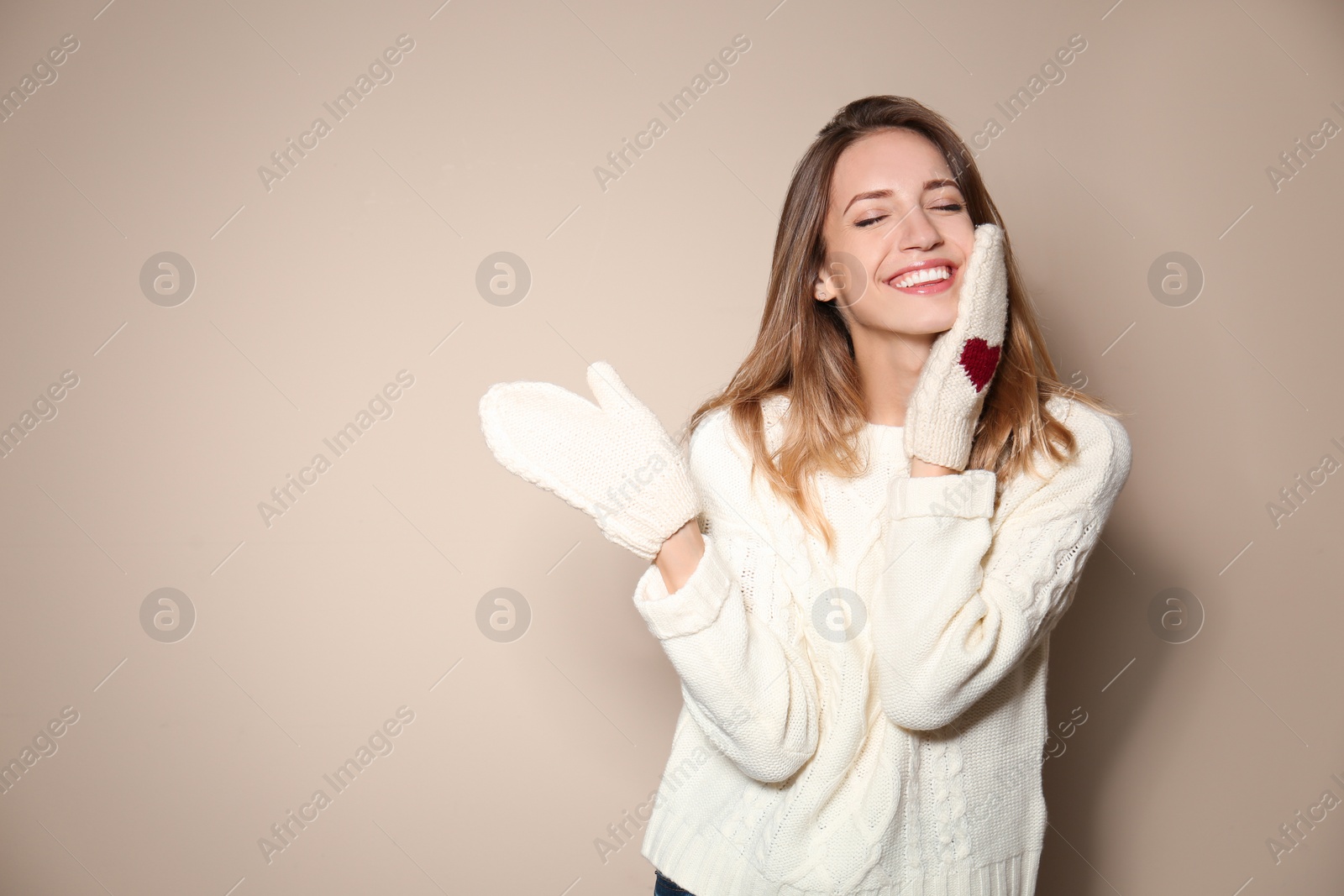 Image of Happy young woman wearing warm sweater and knitted mittens on beige background 