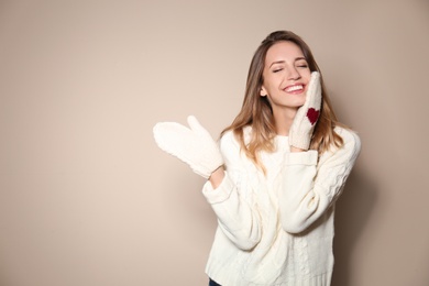 Happy young woman wearing warm sweater and knitted mittens on beige background 