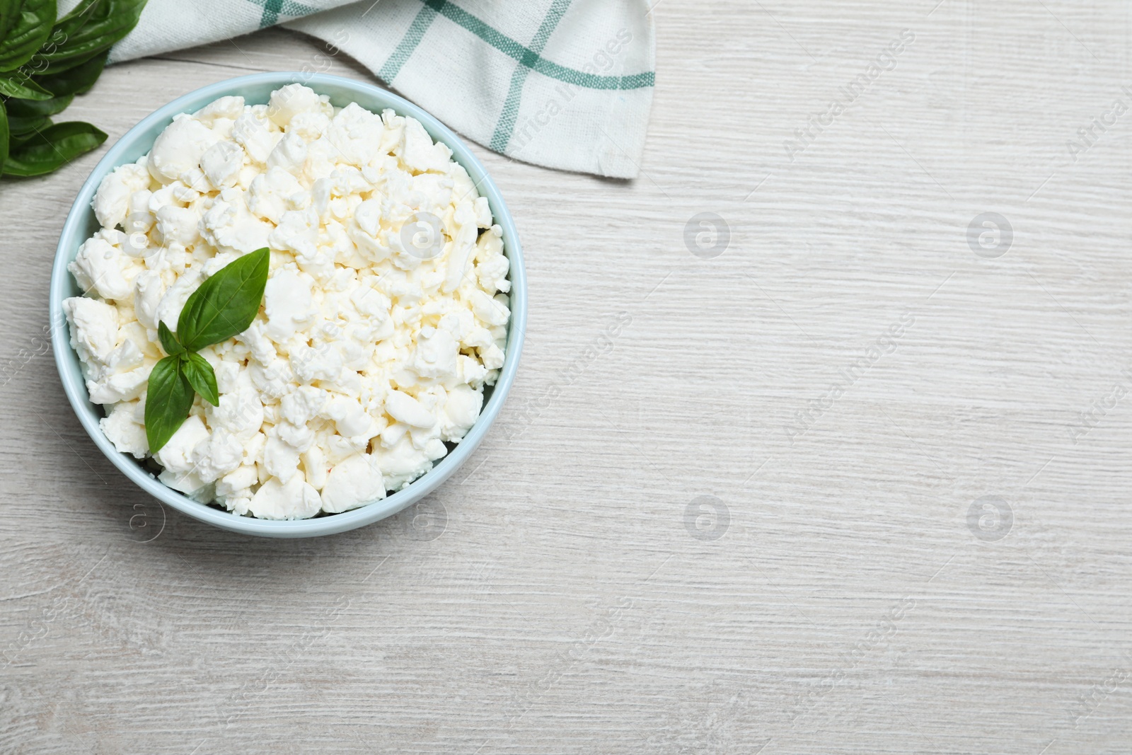 Photo of Fresh cottage cheese with basil in bowl on light wooden table, flat lay. Space for text