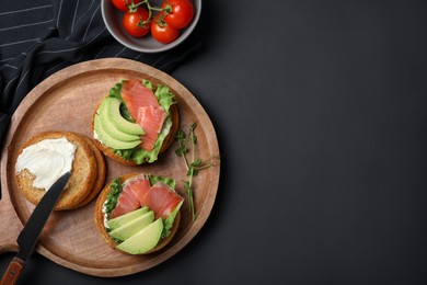 Photo of Tasty rusks with salmon, cream cheese and avocado served on black table, flat lay. Space for text