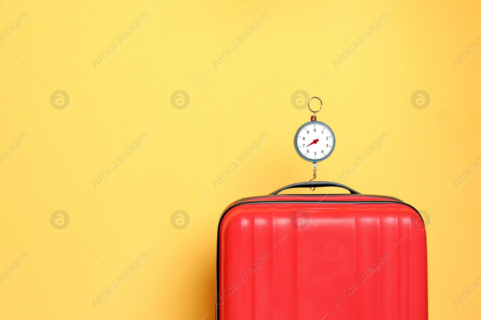 Photo of Modern suitcase and hanging scales against color background, space for text