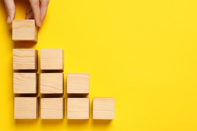 Photo of Woman holding wooden cube near others on yellow background, top view and space for text. Management concept