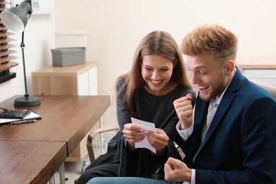 Happy young people with lottery ticket in office