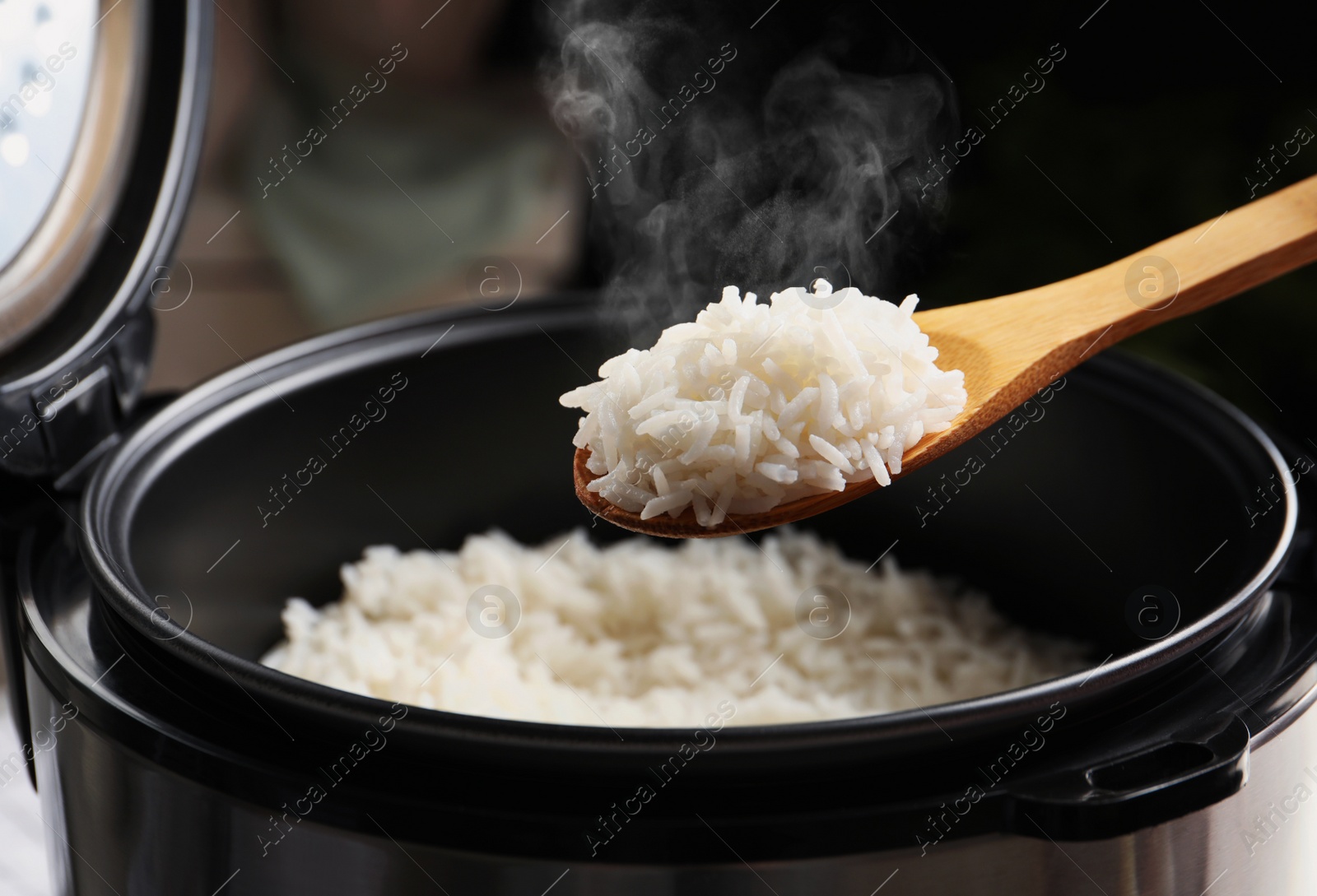 Image of Spoon with tasty hot rice over cooker, closeup