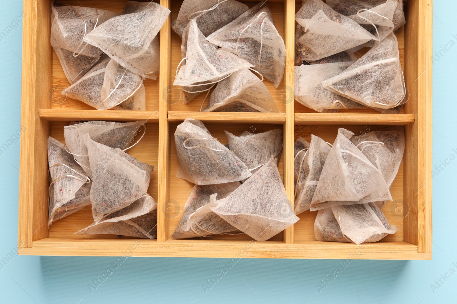 Photo of Many tea bags in wooden box on light blue background, flat lay