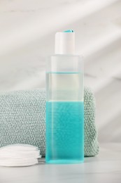 Photo of Bottle of micellar water, towel and cotton pads on white table against marble background