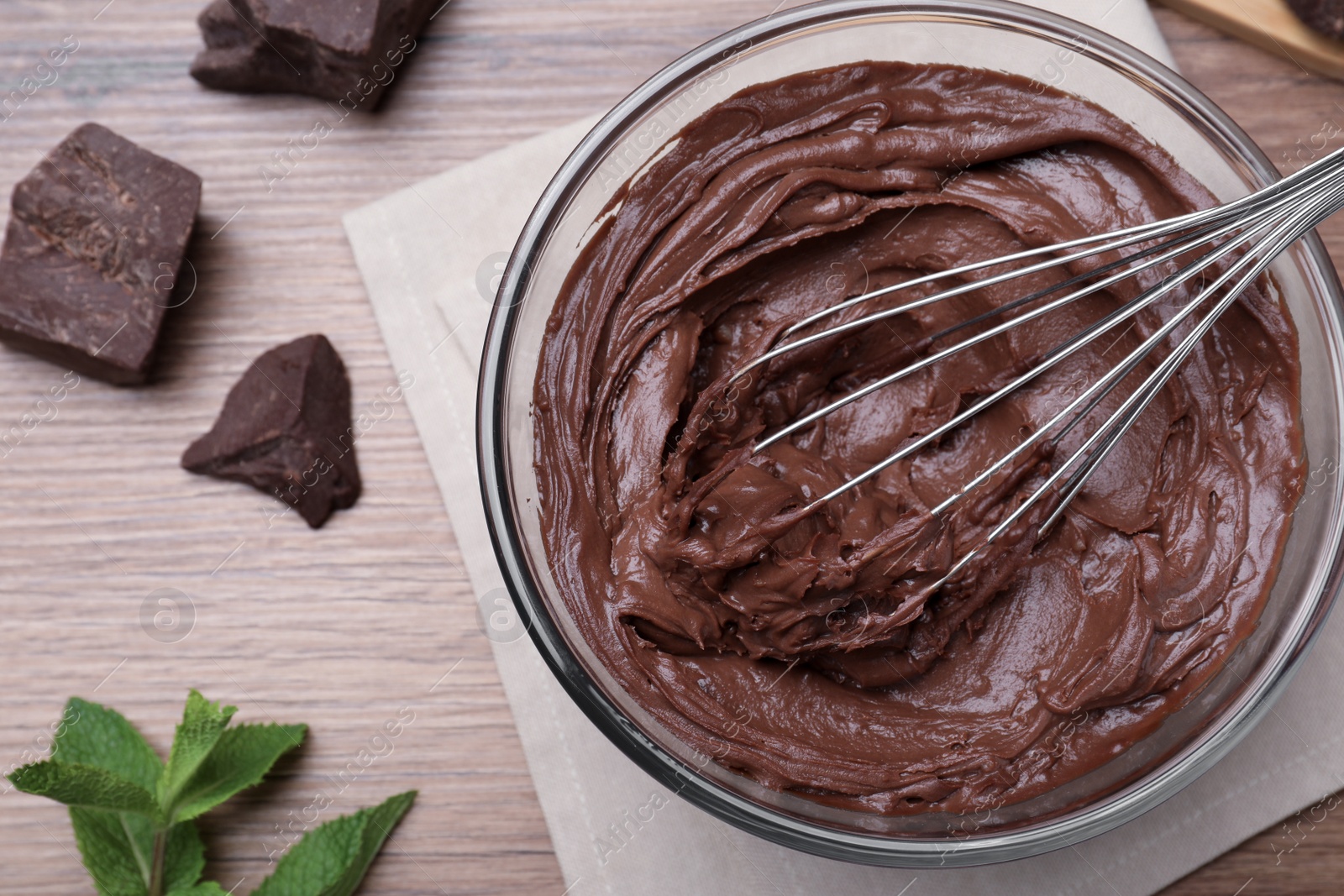 Photo of Whipping chocolate cream with balloon whisk on wooden table, flat lay