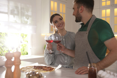 Photo of Lovely young couple drinking wine while cooking together in kitchen