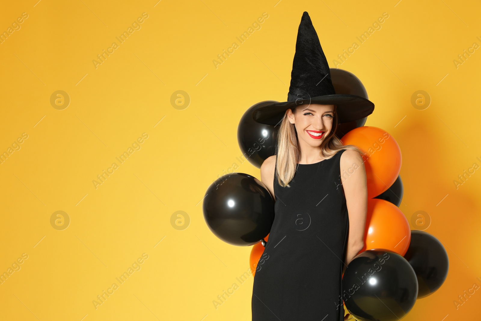 Photo of Beautiful woman wearing witch costume with balloons for Halloween party on yellow background, space for text