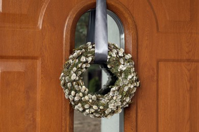 Photo of Wreath made of beautiful willow branches hanging on wooden door