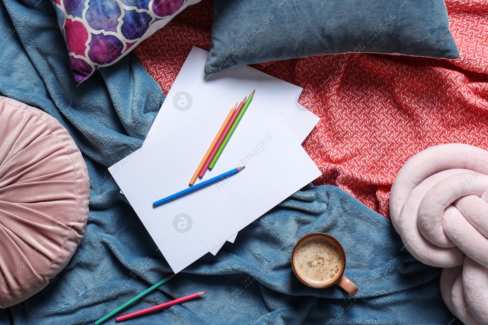 Photo of Flat lay composition with cup of coffee, pencils, pillows and plaid on bed