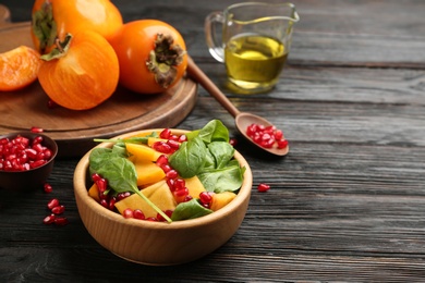 Photo of Delicious persimmon salad with pomegranate and spinach on wooden table. Space for text