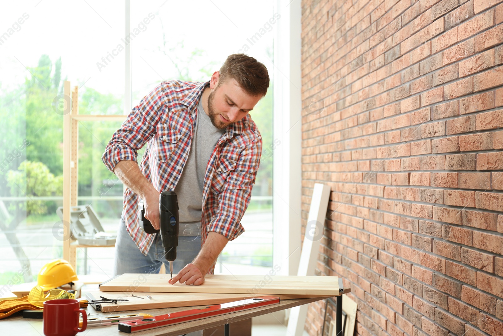 Photo of Young man working with electric screwdriver near brick wall