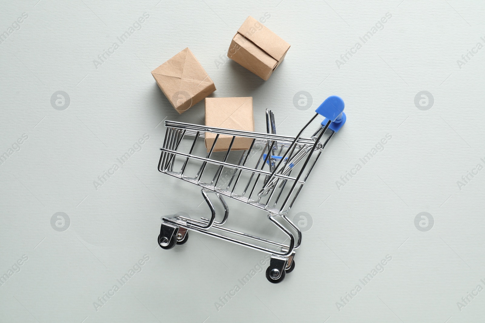 Photo of Small metal shopping cart with cardboard boxes on light background, top view