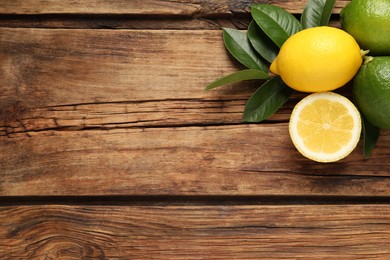 Fresh ripe lemons, lime and green leaves on wooden background, flat lay. Space for text