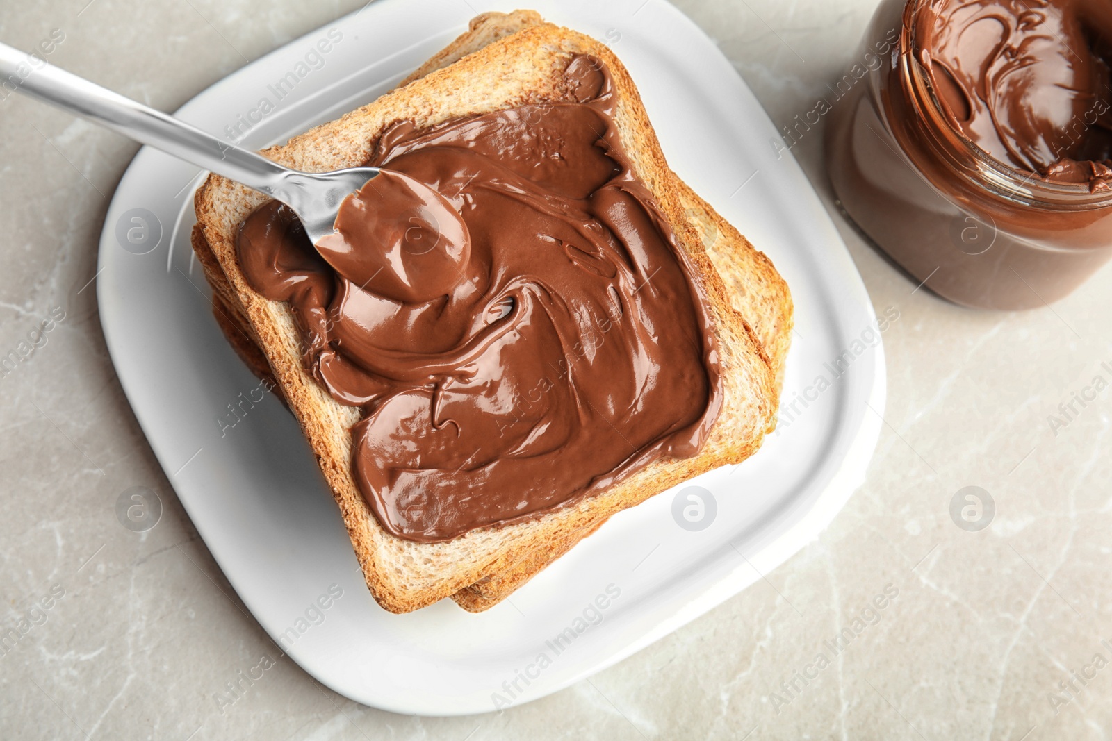 Photo of Spreading sweet chocolate cream onto toast on table, top view