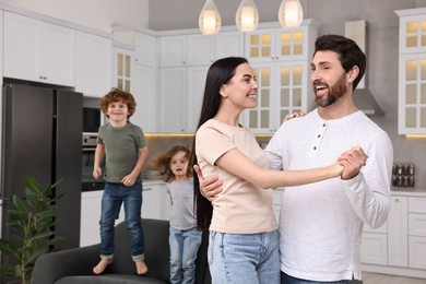 Happy family having fun at home. Couple dancing while children jumping on sofa