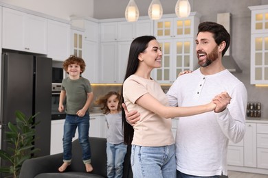 Photo of Happy family having fun at home. Couple dancing while children jumping on sofa