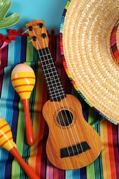 Photo of Mexican sombrero hat, maracas and ukulele on light blue table, flat lay