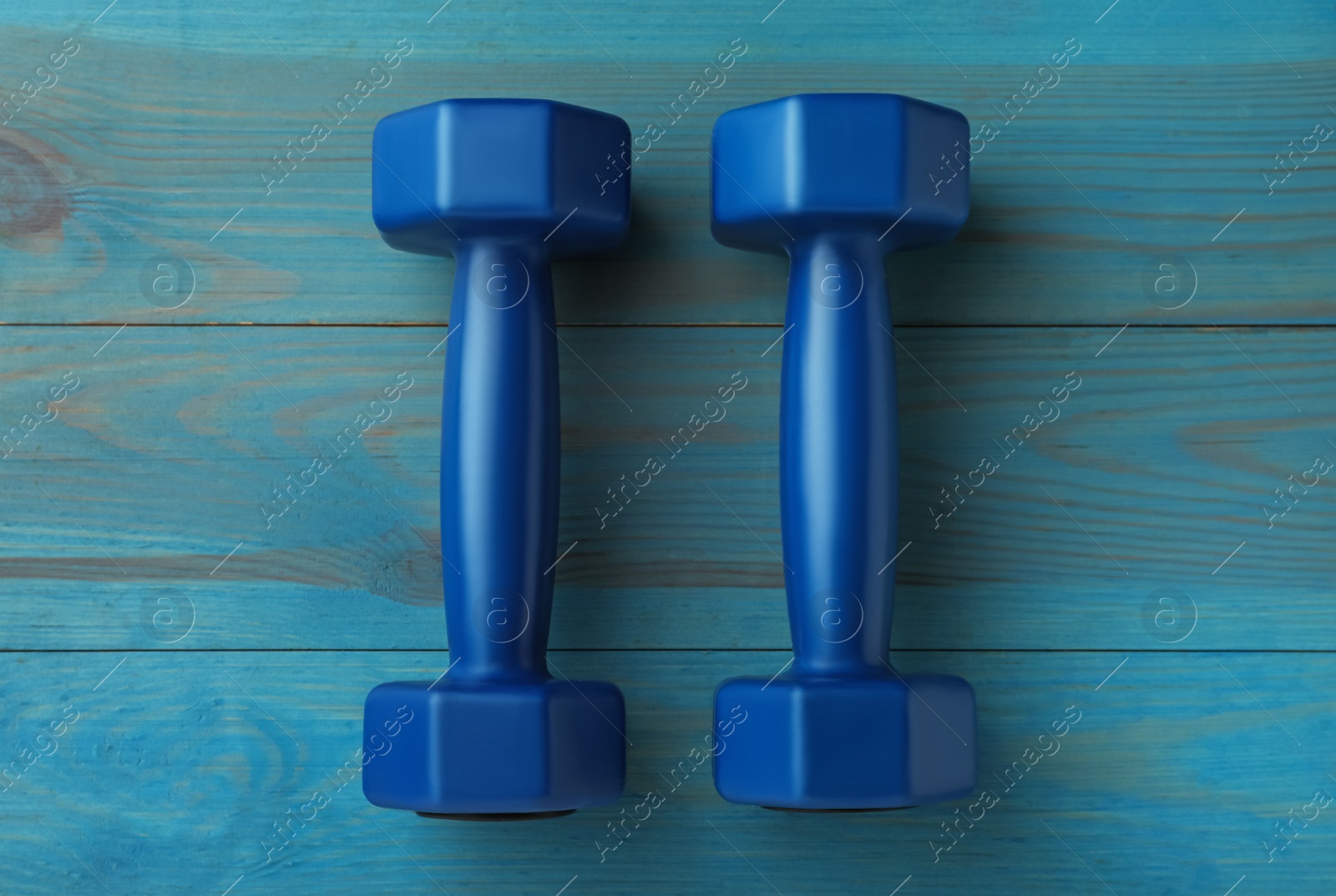 Photo of Blue dumbbells on turquoise wooden table, flat lay