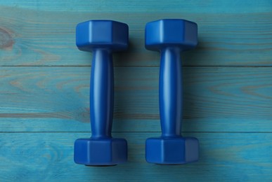 Photo of Blue dumbbells on turquoise wooden table, flat lay