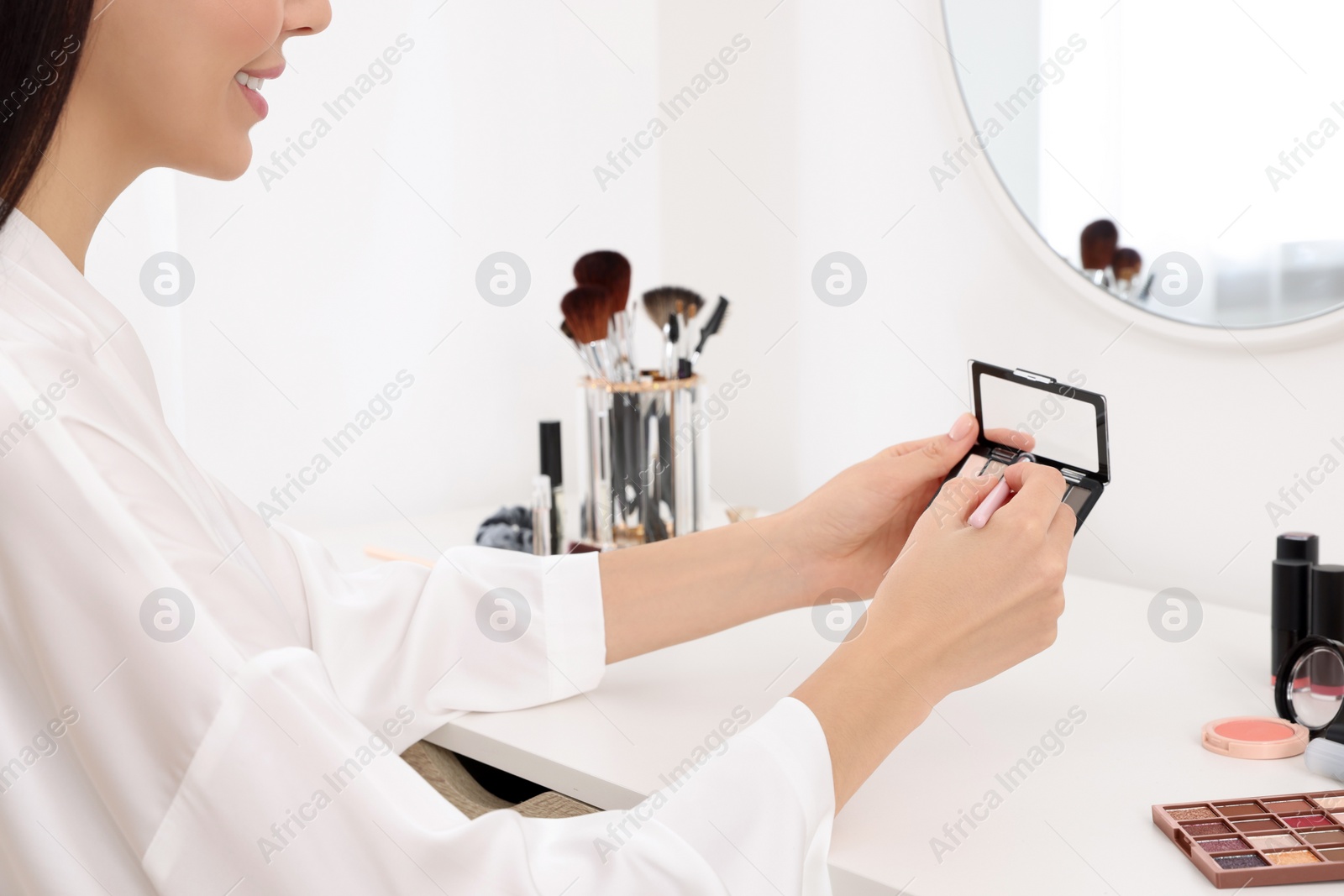 Photo of Woman with eyeshadow palette and brush at dressing table, closeup