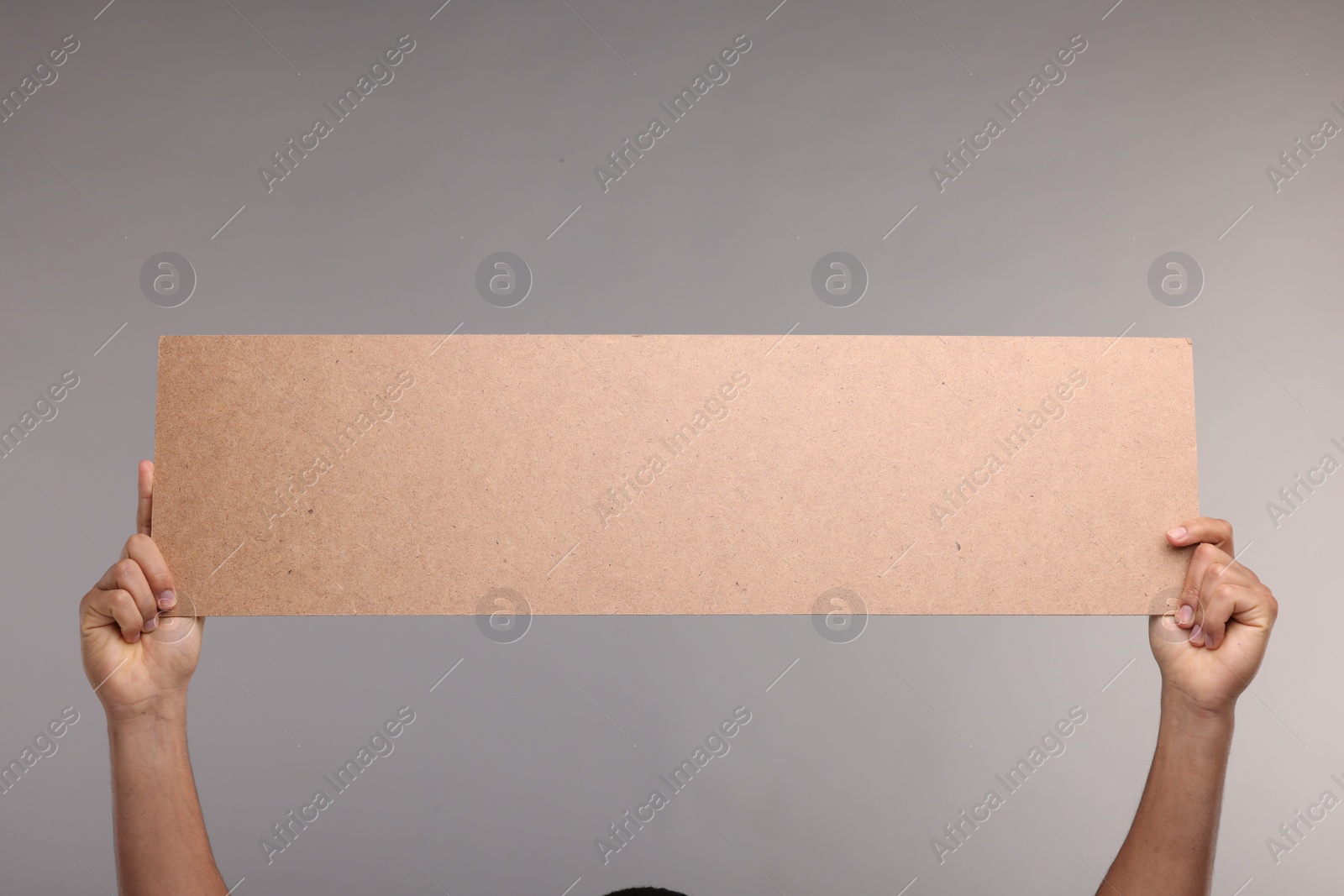 Photo of Man holding blank cardboard banner on grey background, closeup. Space for text