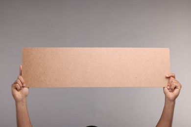 Photo of Man holding blank cardboard banner on grey background, closeup. Space for text